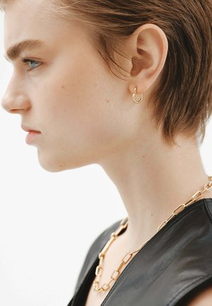 Pendiente de aro de oro con una forma única. Parte superior de cuero negro con un collar de cadena que presenta eslabones alargados. Textura suave, diseño minimalista.