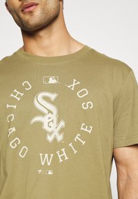 Olivově zelené bavlněné tričko s velkým bílým logem Chicago White Sox a textem v kruhovém vzoru, krátk�é rukávy a kulatý výstřih.