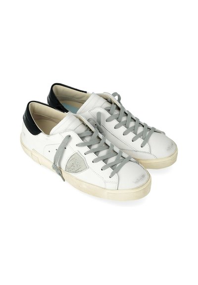 Baskets blanches basses avec des lacets gris, des languettes de talon noires et des semelles usées sur un fond blanc uni.