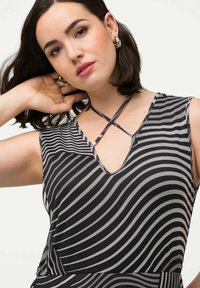 Vestido sin mangas de rayas blancas y negras con escote en V y tirantes entrelazados. El material parece ligero y texturizado. Presenta una silueta ajustada.