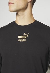 Felpa nera con colletto rotondo, con logo dorato "PUMA KING" e grafica di un puma in salto sul petto. Tessuto morbido.