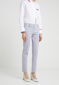 Světle šedé kalhoty na míru s úzkým střihem, které se vyznačují hladkou texturou a čistými liniemi. Nesené s bílou košilí a bílými lodičkami.