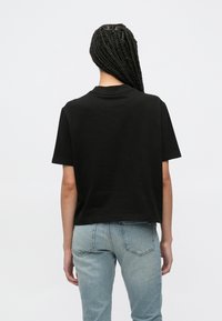 Μαύρο βαμβακερό κοντομάνικο μπλουζάκι με άνετη εφαρμογή, στρογγυλή λαιμόκοψη και ελαφρώς κοντή γραμμή, σε συνδυασμό με ανοιχτόχρωμο μπλε τζιν.