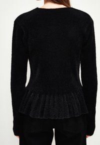 Czarny sweter o miękkim, teksturowanym wykończeniu. Posiada żebrowany wzór i peplum na dole. Długie rękawy; widok z tyłu.