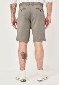 Graue gewebte Shorts mit tailliertem Schnitt, zwei Gesäßtaschen mit Knöpfen und kontrastierender Naht. Kombiniert mit weißen Sneakers im High-Top-Stil.
