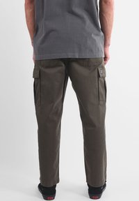 Pantalon cargo en tissu mélangé coton, de couleur vert olive, doté de poches latérales, d'une coupe décontractée et d'ourlets remontés. Associé à une chemise grise.