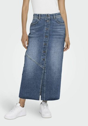 Denim maxi skirt with front button closure, contrast stitching, and side slits. Worn with white sneakers, featuring a fitted waist.