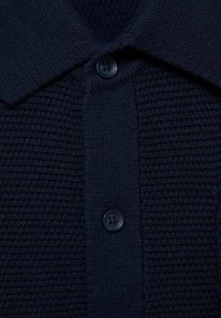 Mörkblå polo skjorta med texturerad stickad tyg, med krage och en knappslå med en mörkblå knapp.