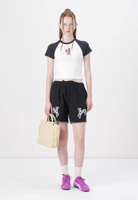 Baltas ir juodas trumpomis rankovėmis trumpas viršus su grafika, derinamas su juodomis šortais su balta siuvinėjimu, baltais kojinėjais ir purpuriniais sportbačiais.