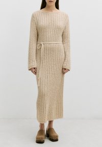 Beige gestricktes langes Kleid mit einem strukturierten Muster, weiten Ärmeln und einem passenden Kordelgürtel in der Taille, kombiniert mit braunen Clogs.