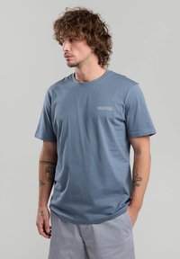 Blue short-sleeve t-shirt made of cotton, features a crew neckline and "WAVES" embroidered in light gray on the chest. Smooth texture.