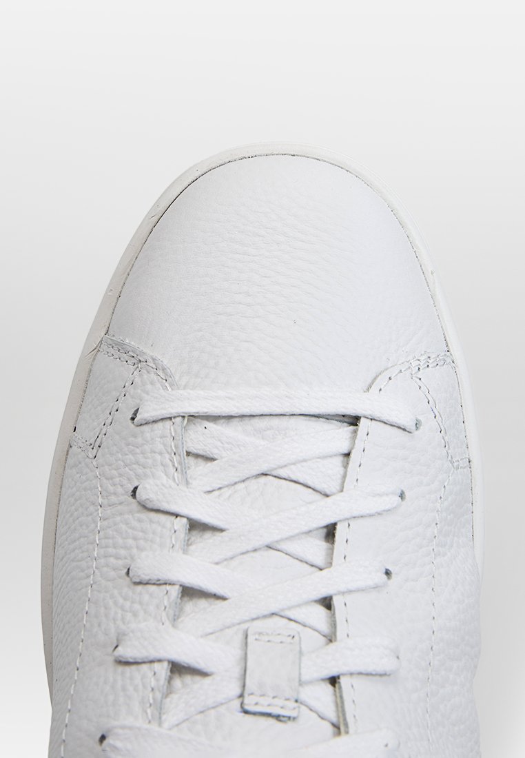 Baskets en cuir blanc avec surface texturée, bout rond, lacets plats et design minimaliste. Présente une semelle en caoutchouc solide et des coutures discrètes.