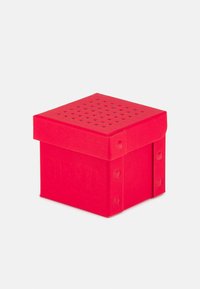 Boîte de rangement carrée rouge avec un couvercle perforé et un logo en relief. Fabriquée à partir d'un matériau durable, elle présente des coins arrondis et des accents de quincaillerie visibles.