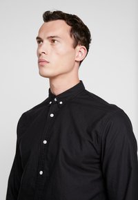 Zwarte button-up shirt van katoen met een textuurafwerking, witte knopen en een klein logo geborduurd op de linkerborst.