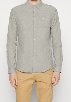 Camisa de botones de manga larga de color gris claro con cuello y pequeño logotipo en el pecho, hecha de tejido texturizado. Botones en la parte delantera.