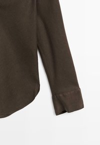 Chemise à manches longues marron foncé avec poignet et ourlet courbé, présentée sur un fond blanc.