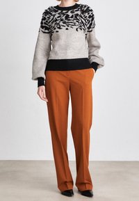 Knitted sweater in beige with black abstract pattern, featuring puffed sleeves and a ribbed black waistband, paired with high-waisted orange trousers.