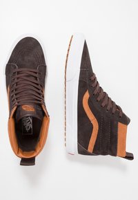 Braune Wildleder-Mid-Top-Sneakers mit orangenen Akzenten, weißer Gummisohle und braunen Schnürsenkeln. Verfügen über ein Logo auf der Zunge und eine strukturierte Oberseite.