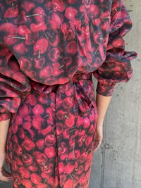 Rochie roșie și neagră cu un model de cireșe, cu mâneci bufante, talie legată și un design fluid, realizată dintr-un material ușor.