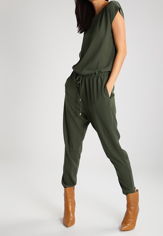 Ensemble deux pièces vert olive comprenant un haut ample avec des manches courtes et un pantalon tapered à taille élastique, associé à des bottes à cheville beiges.