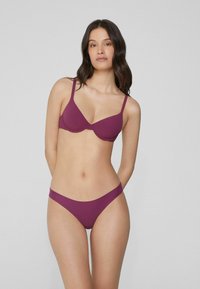 Soutien-gorge violet et culotte assortie en tissu lisse. Le soutien-gorge est doté d'armatures et de bretelles ajustables. L'ensemble présente un design minimaliste sans motifs visibles.