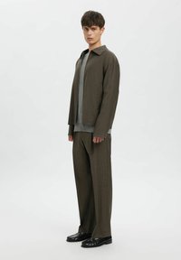 Brūna faktūras žakete pār pelēku džemperi, kopā ar saskaņotām brūnām biksēm. Melni loaferi noslēdz izskatu. Vienkāršs, atslābināts dizains.