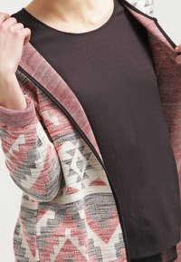 Mønstret cardigan med geometriske designs i rød, grå og krem, med en blød tekstur og en sort indertop. Åben foran.