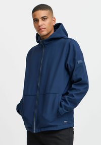 Veste à capuche bleu marine avec fermeture éclair, poches avant, tissu doux et texturé, et patch logo sur la manche. Offre une coupe décontractée.