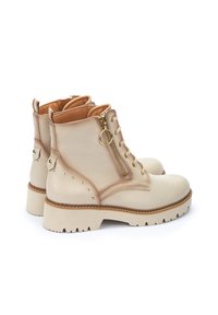 Botas de cuero beige hasta el tobillo con cremalleras laterales, cordones, tachuelas decorativas y una suela resistente. Presenta un detalle de costura marrón a lo largo de la suela.