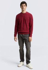 Red textured sweater with a crew neckline, paired with dark jeans and white sneakers. Simple design, no visible patterns or logos.