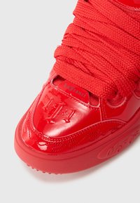 Sneaker rosso brillante con lacci spessi, finitura lucida, testo "LaFrance" in rilievo, cuciture decorative e dettagli del suola texturizzati.