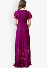 Langes, fuchsienfarbiges Spitzenkleid mit kurzen Ärmeln und komplizierten Blumenmustern. Durchsichtiger unterer Teil, der die Beine darunter enthüllt.