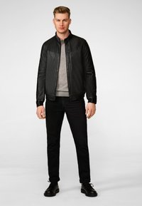 Black leather bomber jacket with a stand collar, zip front, and tonal stitching; paired with gray sweater and black denim jeans.
