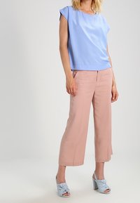 Jasnoniebieska bluzka z krótkim rękawem w połączeniu z różowymi spodniami typu wide-leg. Obuwie ma jasnoniebieski wzór w formie węzła oraz masywny obcas.