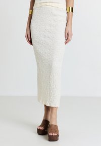 Jupe midi blanche texturée avec un design froissé, assortie à des sandales compensées marron à large sangle et accents dorés.