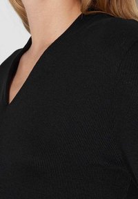 Svart ribbad stickad topp med V-ringning och en figurnära silhuett. Texturen är slät med vertikal ribbning för extra detalj.