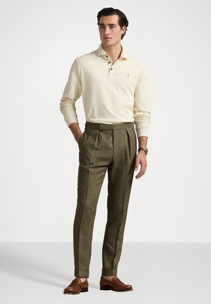 Crème lange mouwen polo met drie knopen, gecombineerd met een bruine geblokte broek. Bruine leren instapschoenen maken de look compleet.