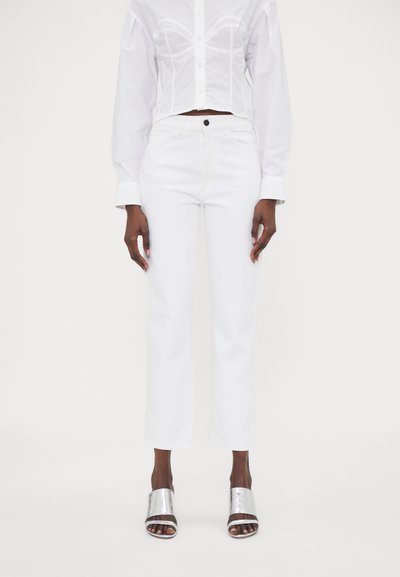 Pantalon en denim blanc avec une coupe droite, présentant une taille haute, des coutures minimales et une fermeture à un bouton. Porté avec des chaussures métalliques à bouts ouverts.