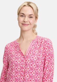 Rosa gemusterte Bluse mit geometrischem Design und floralen Akzenten, einer geknöpften Knopfleiste und einem leicht strukturierten Stoff.