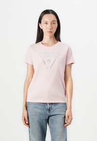 Camiseta de algodón rosa con un gráfico triangular que presenta "GUESS?" en pedrería en el centro. Diseño de mangas cortas y cuello redondo.