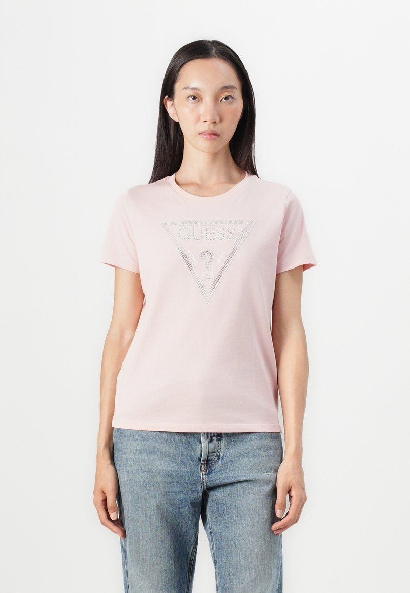 Camiseta de algodón rosa con un gráfico triangular que presenta "GUESS?" en pedrería en el centro. Diseño de mangas cortas y cuello redondo.