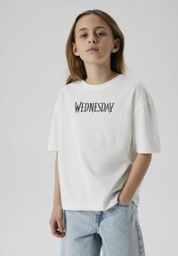 Vit bomull t-shirt med korta ärmar med ordet "ONSDAg" i en svart, stiliserad font. Matchad med ljusblå denimjeans.