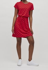 Punainen lyhytnähtävä mekko, jossa on valkoisia pilkkuja, kuminauhalla vyötäröltä kiristetty. Sujuva, kevytsabatti, polviin ulottuva, käytetty valkoisten tennareiden kanssa.