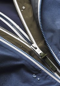 Water-resistant jacket featuring a multi-colored interior with navy, olive, and gray fabrics. Notable zippers in contrasting colors with water droplets.