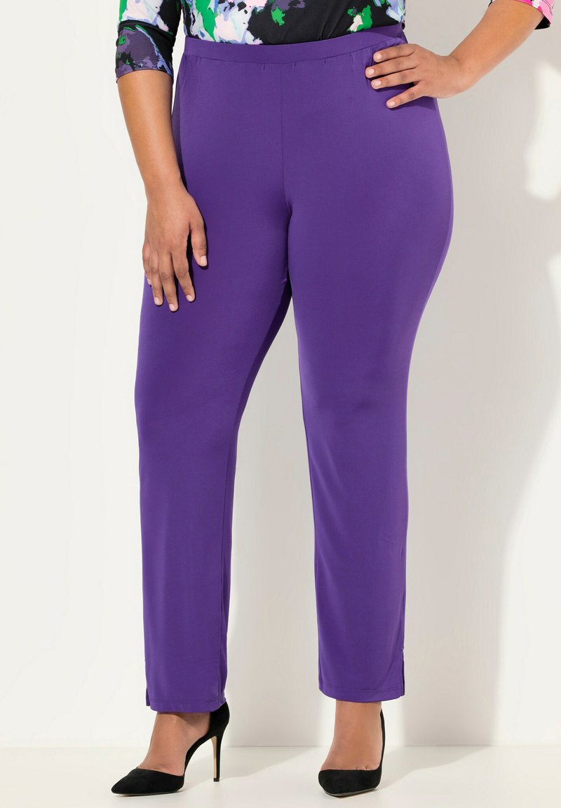 Fialové legíny s hladkou texturou, zúženým střihem a elastickým pasem. Oblečené s černými vysokými podpatky, které předvádějí elegantní design.