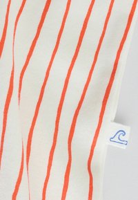 Tissu blanc avec des rayures verticales orange et une petite étiquette blanche portant une icône de vague bleue sur le bord.