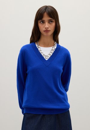 Maglione blu royal a V, lavorato a maglia, maniche lunghe, con polsini e orlo a costine, abbinato a una camicia bianca a girocollo e a una collana in argento.