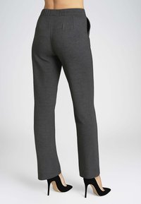Pantaloni grigi slim-fit con una texture liscia, dotati di vita piatta, tasche laterali e gamba affusolata, abbinati a décolleté neri.