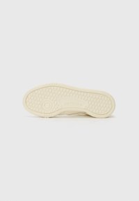Kremfarget såle på sneakers med teksturert gummi, med et sirkulært logo i midten og et diamantmønstret dekk for bedre grep.