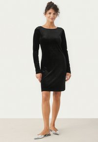Robe longue en velours noir à manches longues, avec un col rond, une silhouette ajustée et une texture lisse, complétée par des chaussures plates argentées.